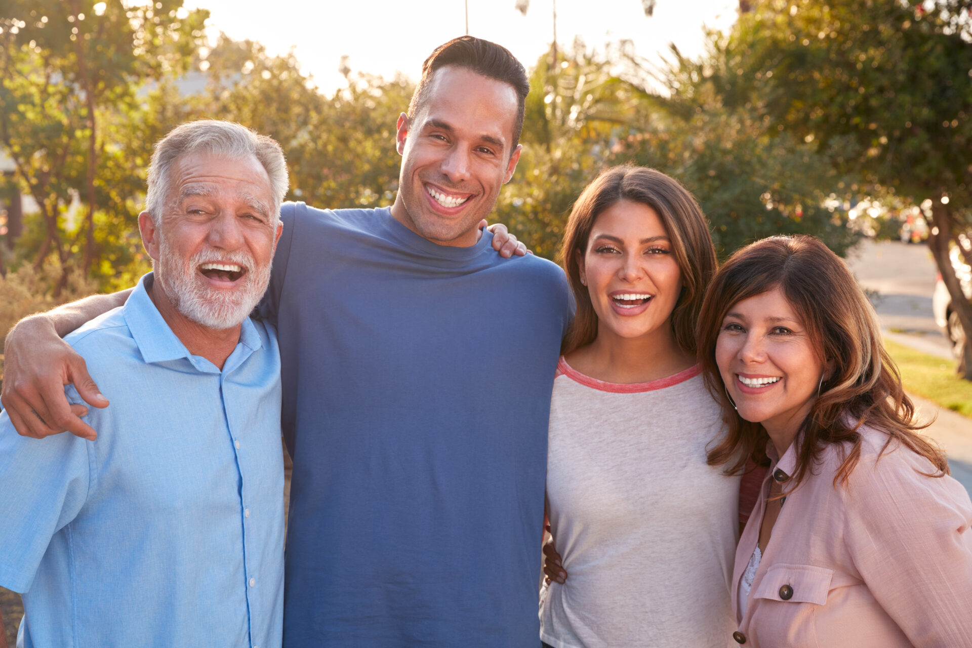 Portrait Of Senior Hispanic Parents With Adult Son And Daughter Relaxing In Garden At Home Together